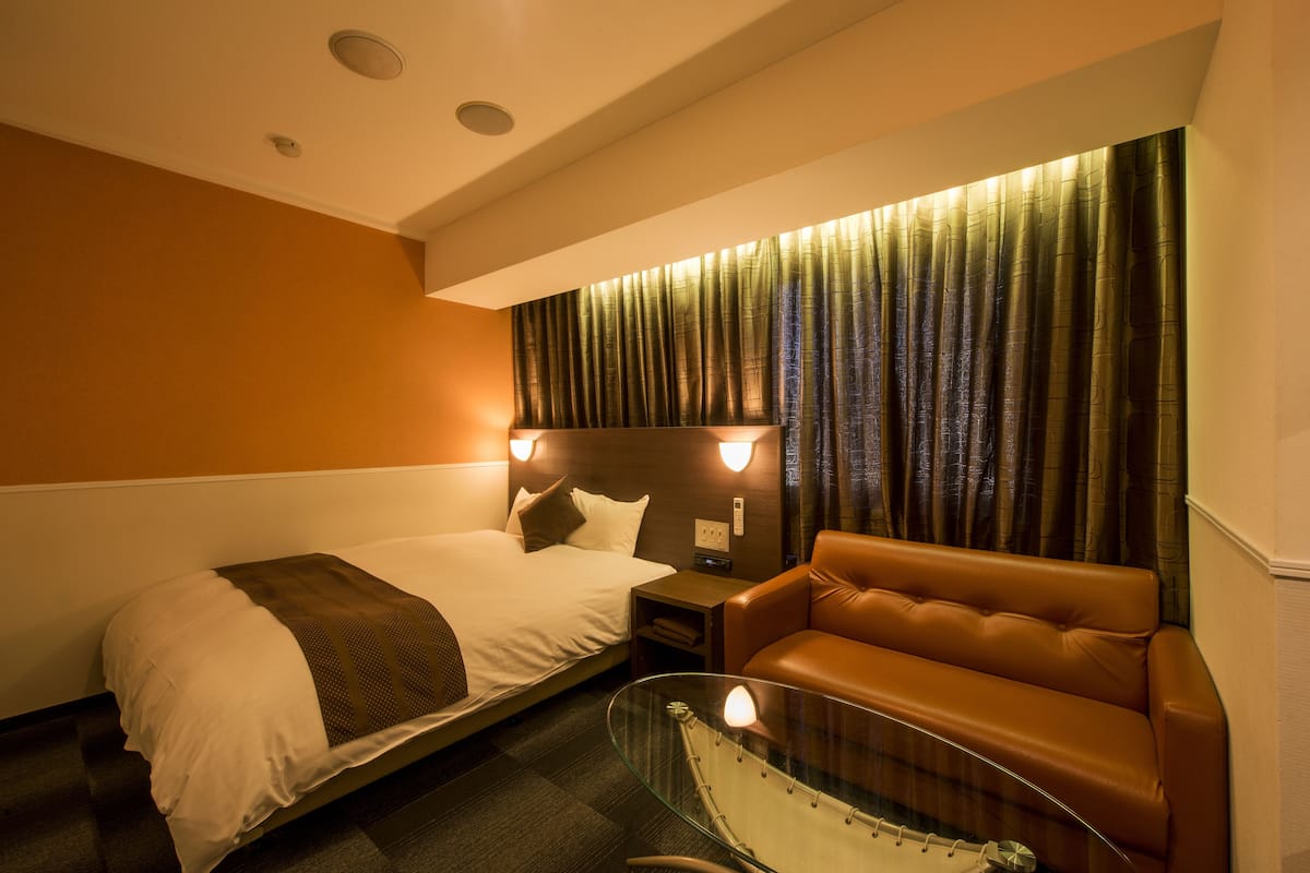 A hotel room with a bed, a glass table, a leather sofa, and a wall-mounted TV.