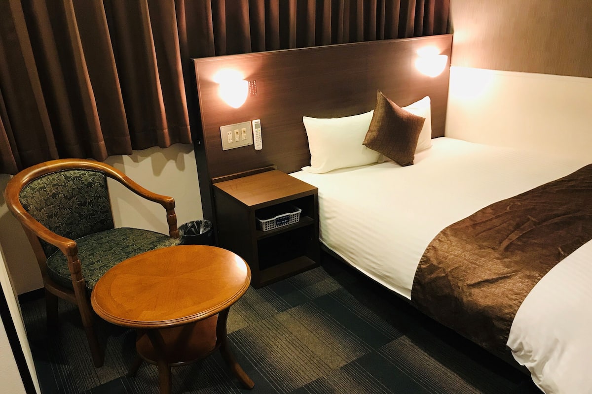 A hotel room with a bed, a chair, a nightstand, and a lamp.