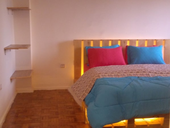 A bedroom with a wooden headboard, a bed with a patterned bedspread, and a wooden floor.