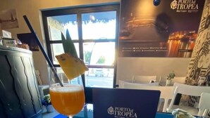 Ett bord med ett glas tropisk drink, en tallrik med skivor av kiwi och ananas samt en skylt med texten Porto de Tropea.