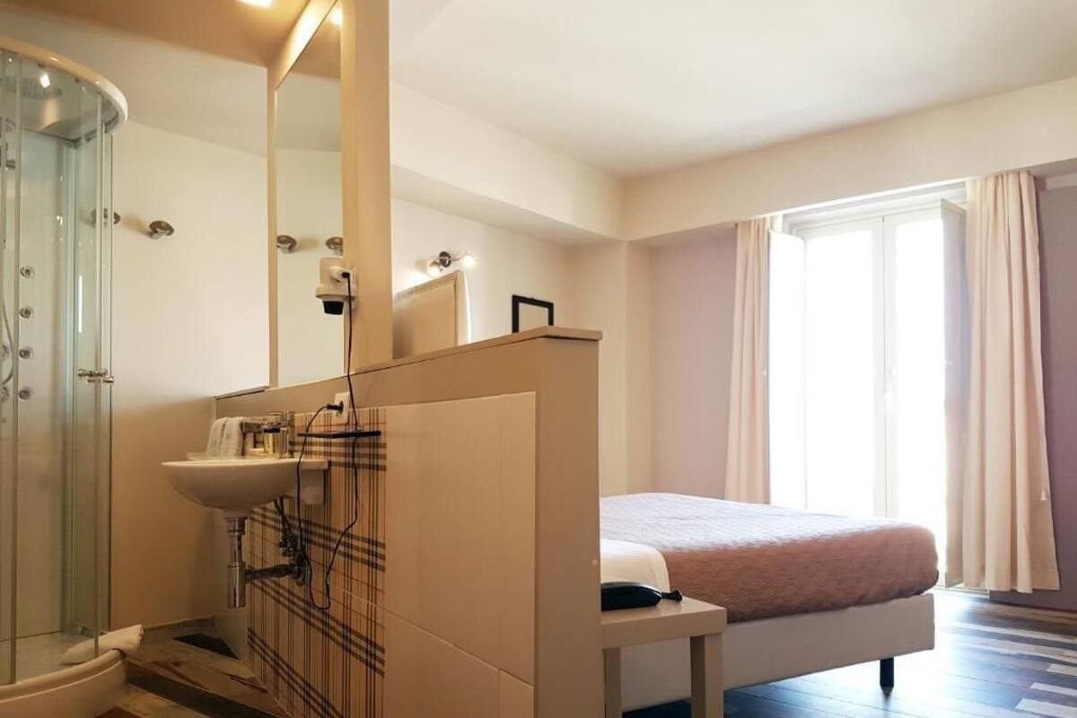 Habitación de hotel con ducha, lavamanos, cama y ventana con cortinas.