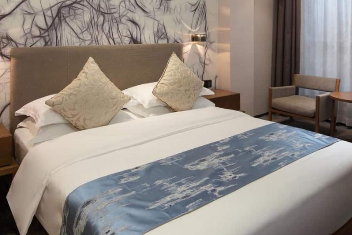 Hotelkamer met een groot bed, twee kussens, een nachtkastje, een stoel en een muur met een afbeelding van een tak.