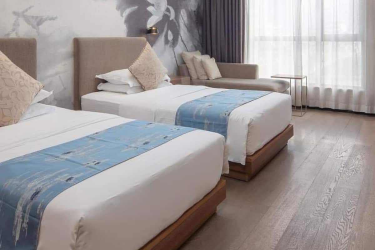 Een hotelkamer met twee bedden, een kleintje tafel en een groot raam met gordijnen.