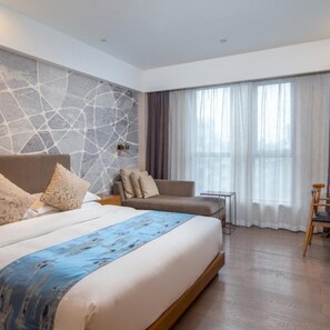 A modern hotel room with a large bed, a seating area, and a view of the outdoors through sheer curtains.