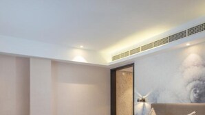 Une chambre moderne avec un grand lit, une table de chevet, une chaise et un mur orné d’une fresque représentant des nuages.