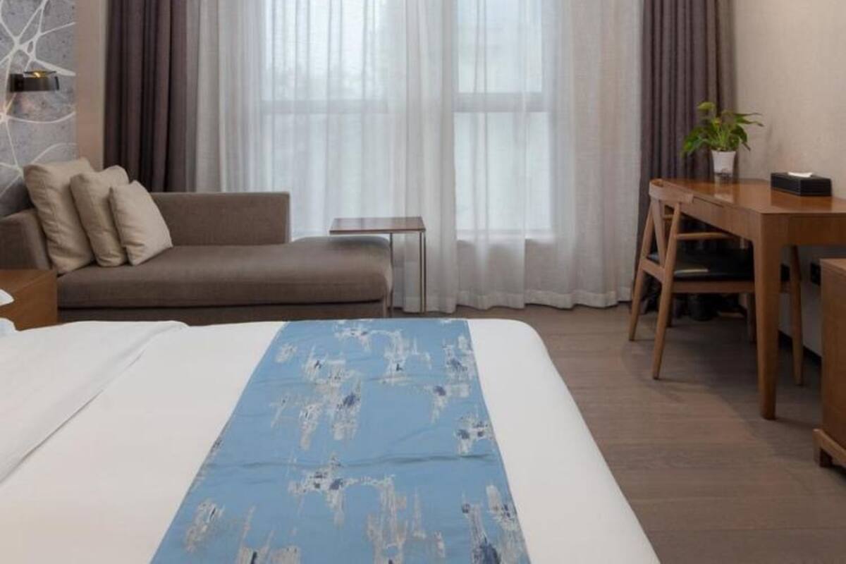 Een moderne hotelkamer met een groot bed, een bank, een bureau en een kamerplant.