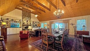 A spacious living area with a high ceiling, wooden beams, a fireplace, and a dining area with a large table and chairs.
