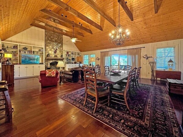A spacious living area with a high ceiling, wooden beams, a fireplace, and a dining area with a large table and chairs. - Three Levels of Pure Mountain | The Blackberry (Highlands)