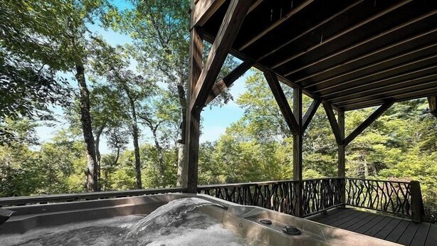A hot tub with a wooden deck and railing, surrounded by trees.