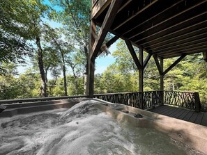 A hot tub with a wooden deck and railing, surrounded by trees. - Three Levels of Pure Mountain | The Blackberry (Highlands)