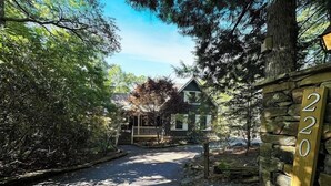 A stone wall with a house number 220, a paved driveway leading to a house with a porch, surrounded by trees and shrubs.