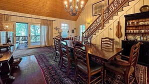 A dining area with a wooden table and chairs, a chandelier, and a staircase with a railing.