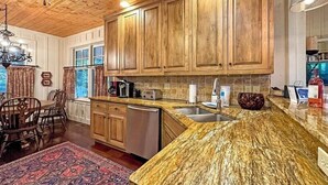 Una cucina con mobili in legno, un piano di lavoro in granito, una lavastoviglie e un'area pranzo con un tappeto e sedie.