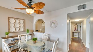 Ein Essbereich mit Glastisch, weißen Stühlen, Deckenventilator und dekorativer Wandgestaltung.