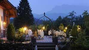 Ein Essbereich im Freien mit gedeckten Tischen, umgeben von Bäumen und einem Bergpanorama.