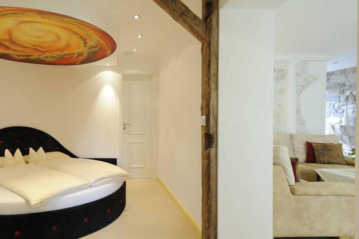 A bedroom with a bed, a ceiling mural, and a view of a living area with a sofa.
