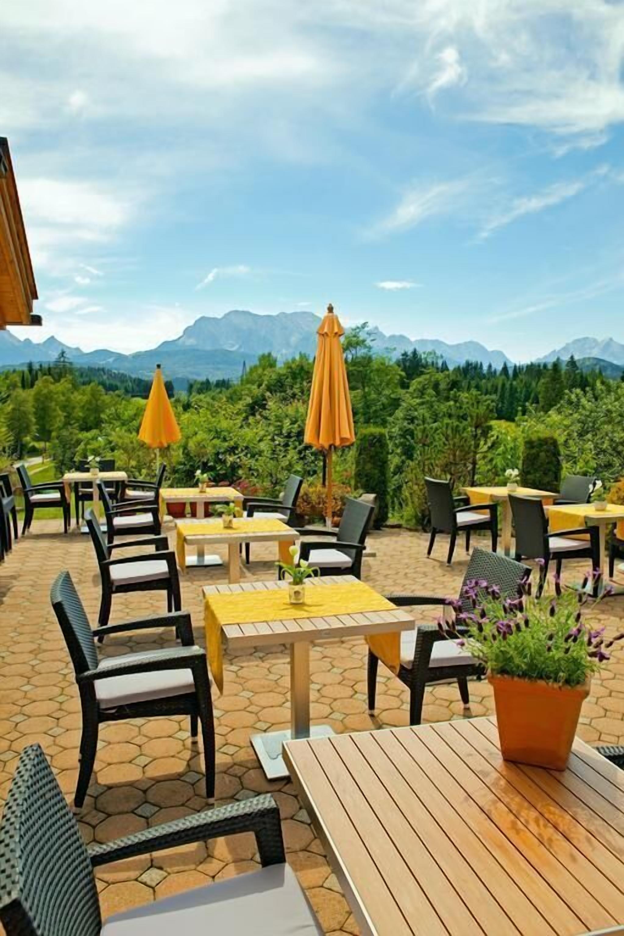 Ein Sitzbereich im Freien mit Tischen und Stühlen, umgeben von einer gebirgigen Landschaft.