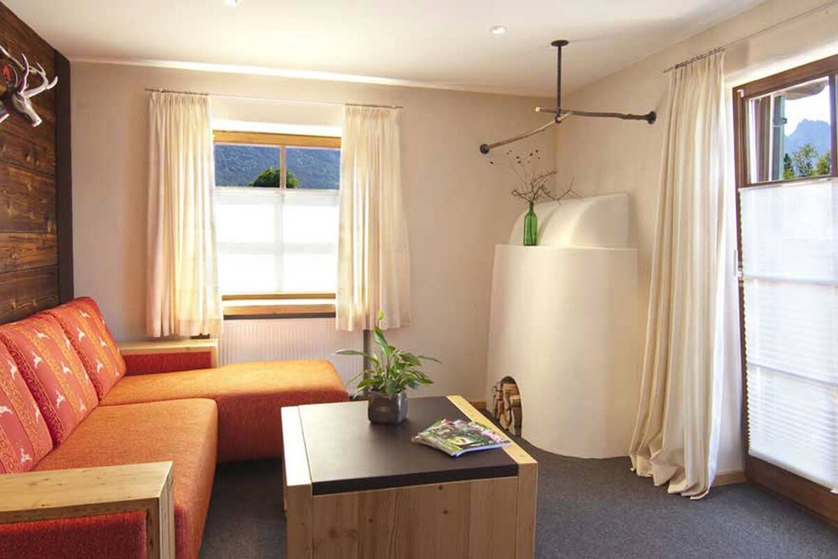 A cozy room with a wooden wall, a red sofa, a small table with a magazine, and a window with curtains.