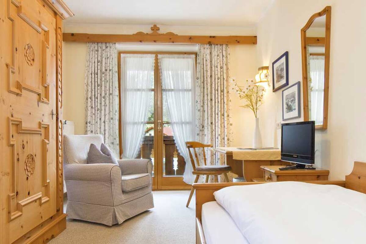 A hotel room with a bed, a desk with a TV, a chair, and a wooden wardrobe.