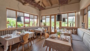 Ein Essbereich mit Holztischen und -bänken, großen Fenstern mit Jalousien und hängenden Pendelleuchten.