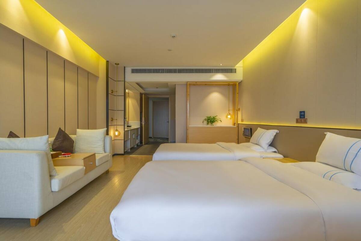 Hotelkamer met een groot bed, een slaapbank en een kleine tafel. Er staat een plant aan de muur en een deur naar de gang.