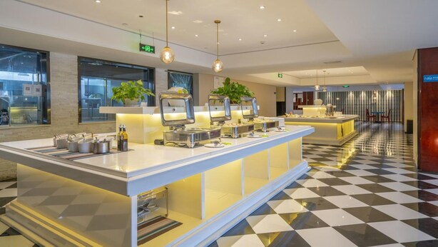 Un moderno vestíbulo de hotel con piso a cuadros, una zona de buffet con diferentes estaciones de comida e iluminación colgante.