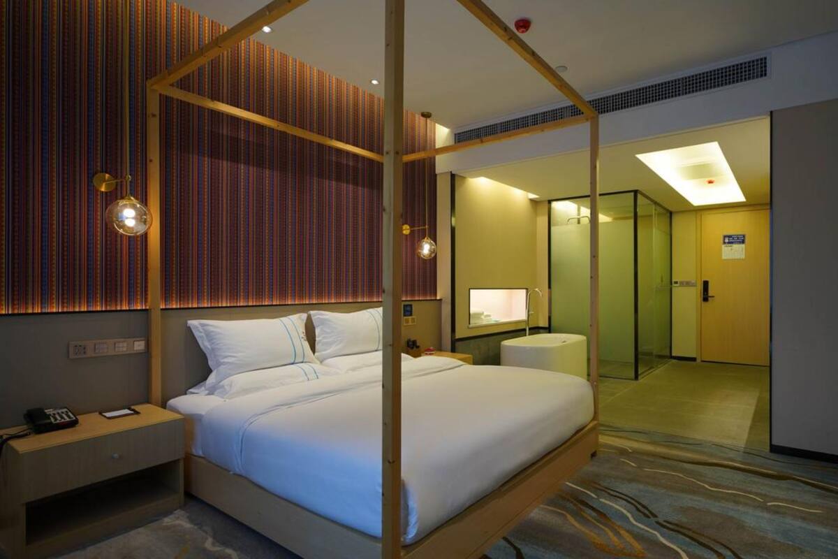 Een hotelkamer met een hemelbed, een nachtkastje met telefoon, een kleine ronde tafel met lamp en een grote spiegel aan de muur.