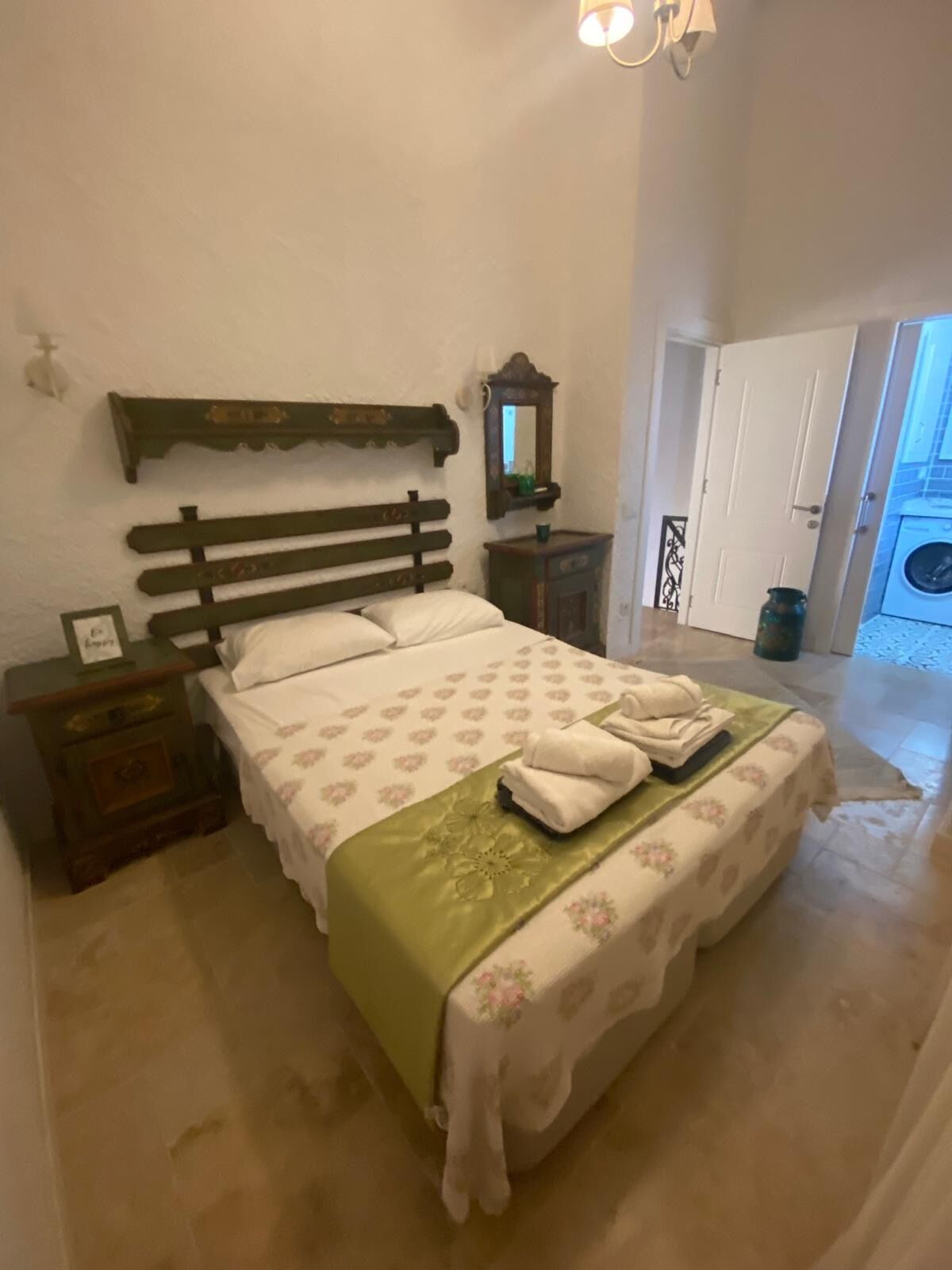 Un dormitorio con una cama, una mesita de noche, un aparador, un espejo y una puerta que da a un área de lavandería.