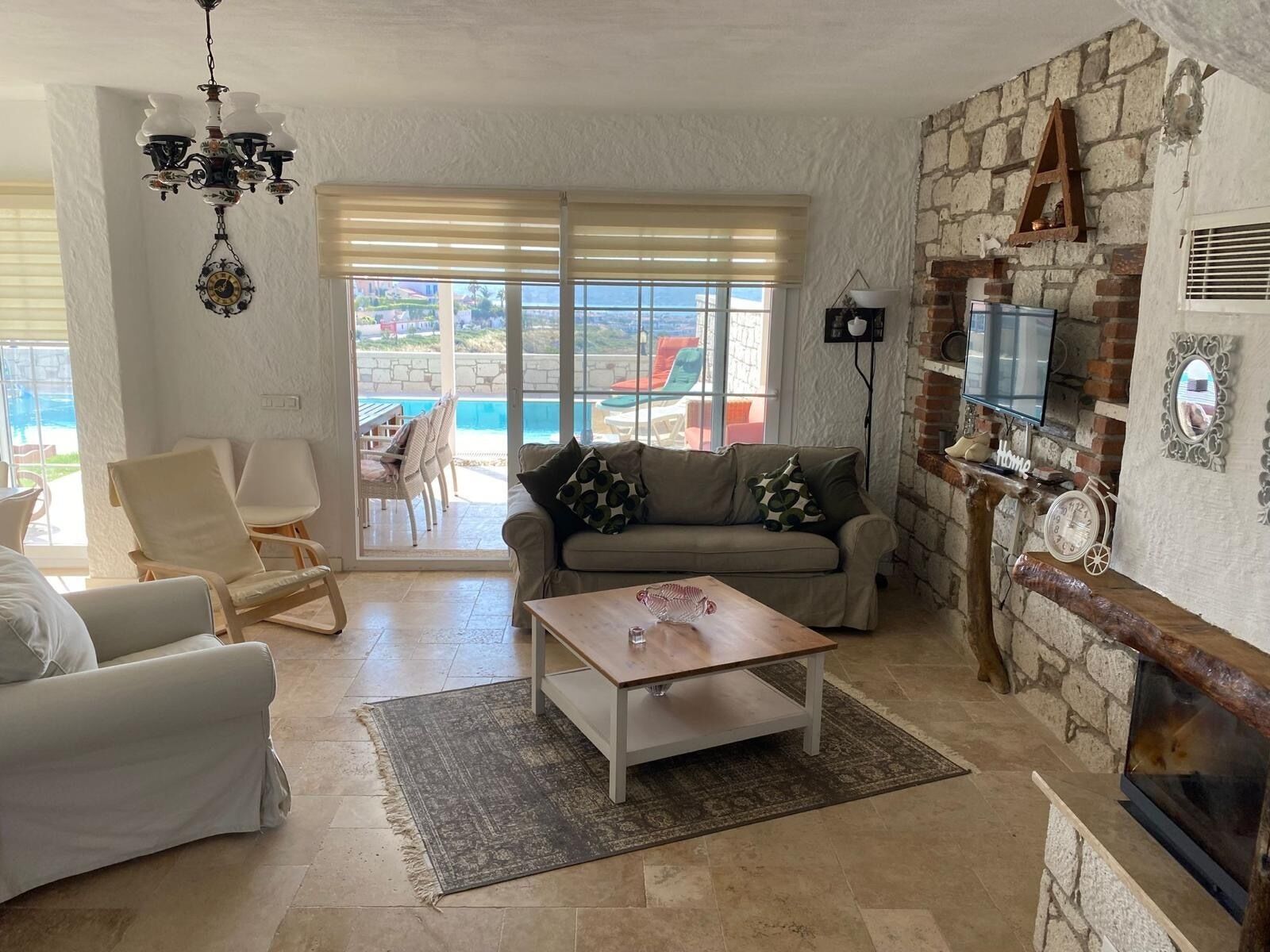 Una sala de estar con sofá, sillas, una mesita de centro, chimenea, televisión y vista a una piscina.
