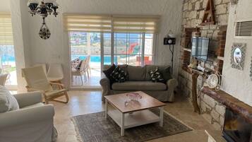 Una sala de estar con sofá, sillas, una mesita de centro, chimenea, televisión y vista a una piscina.