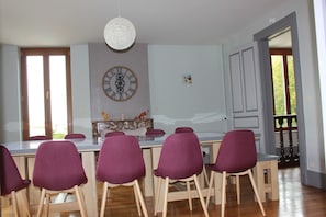 A dining area with a wooden table, purple chairs, a wall clock, and a hanging light fixture.