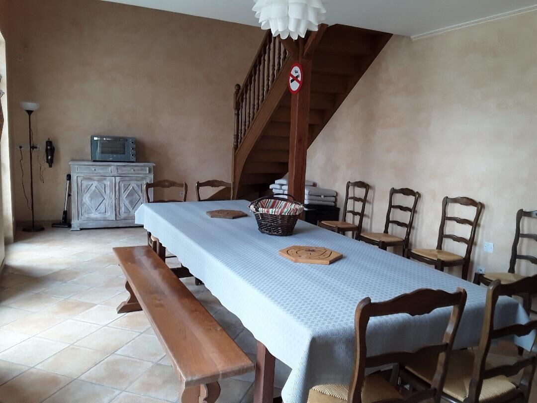 A dining area with a long table, wooden chairs, a bench, a basket, and a microwave on a cabinet.
