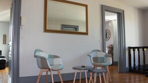 A room with two chairs and a small table, a large mirror on the wall, and a staircase in the background.