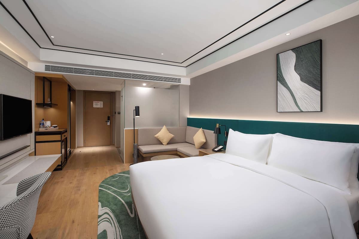 A modern hotel room with a large bed, a desk, a television, and a sofa.