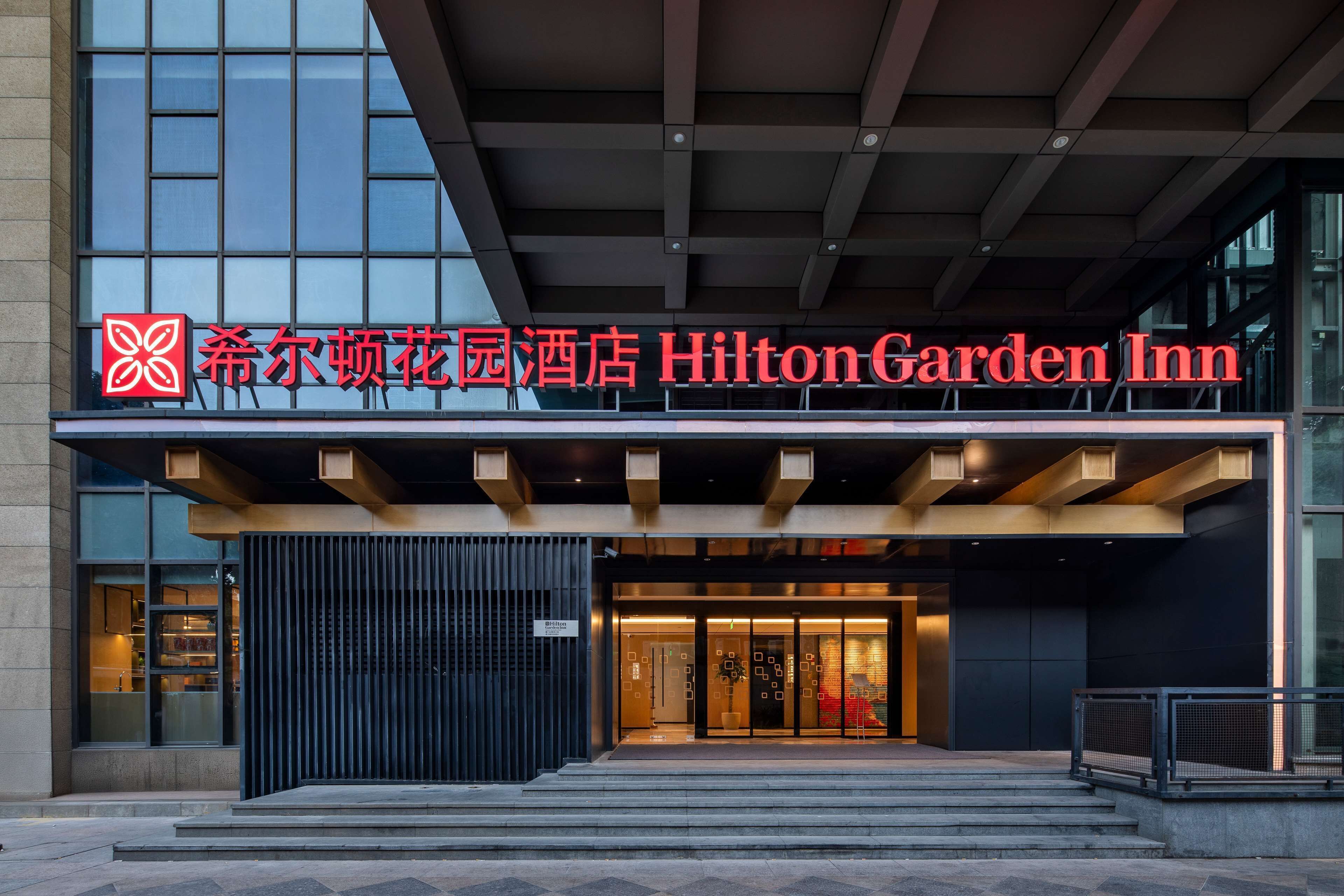 The exterior of Hilton Garden Inn with a modern facade, large glass windows, and a prominent entrance with steps leading up to it.