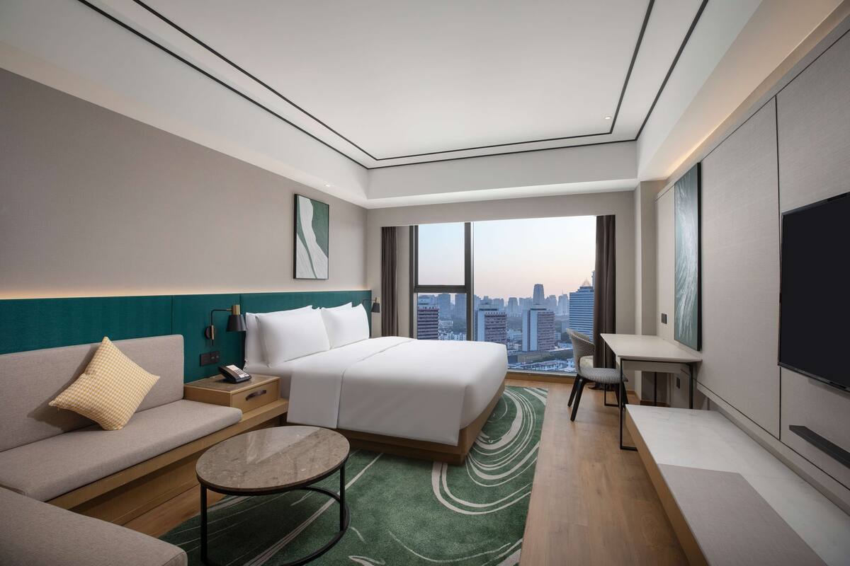A modern hotel room with a bed, sofa, and a desk with a chair.