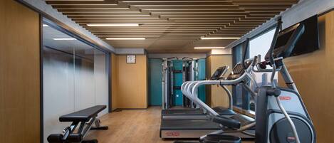 Une salle de sport équipée de tapis de course, de vélos elliptiques et d’un banc de musculation.