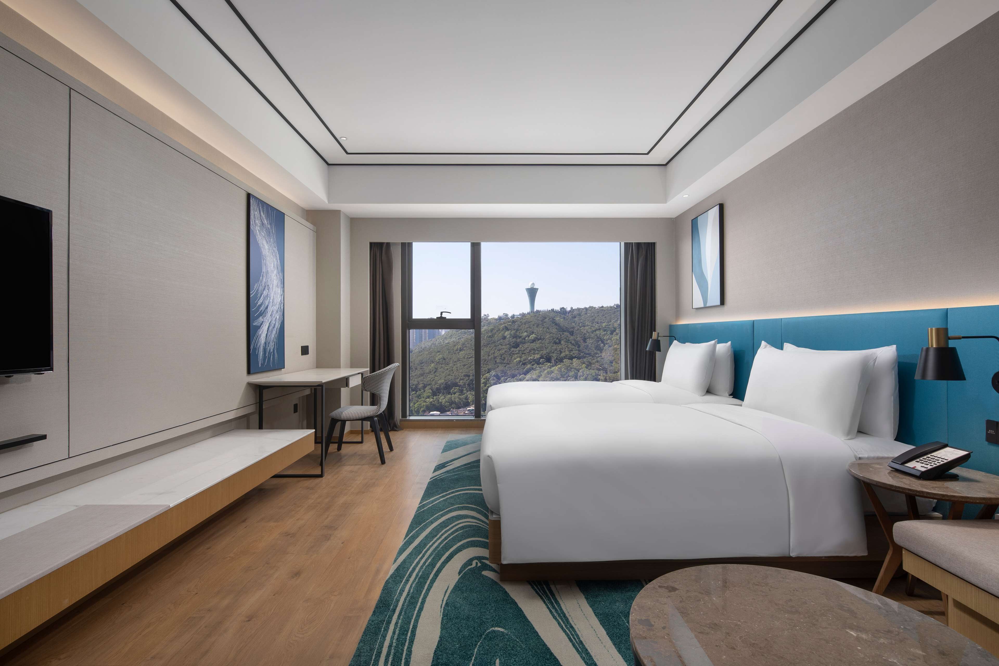 A modern hotel room with a large bed, a desk, and a view of a tower through the window.