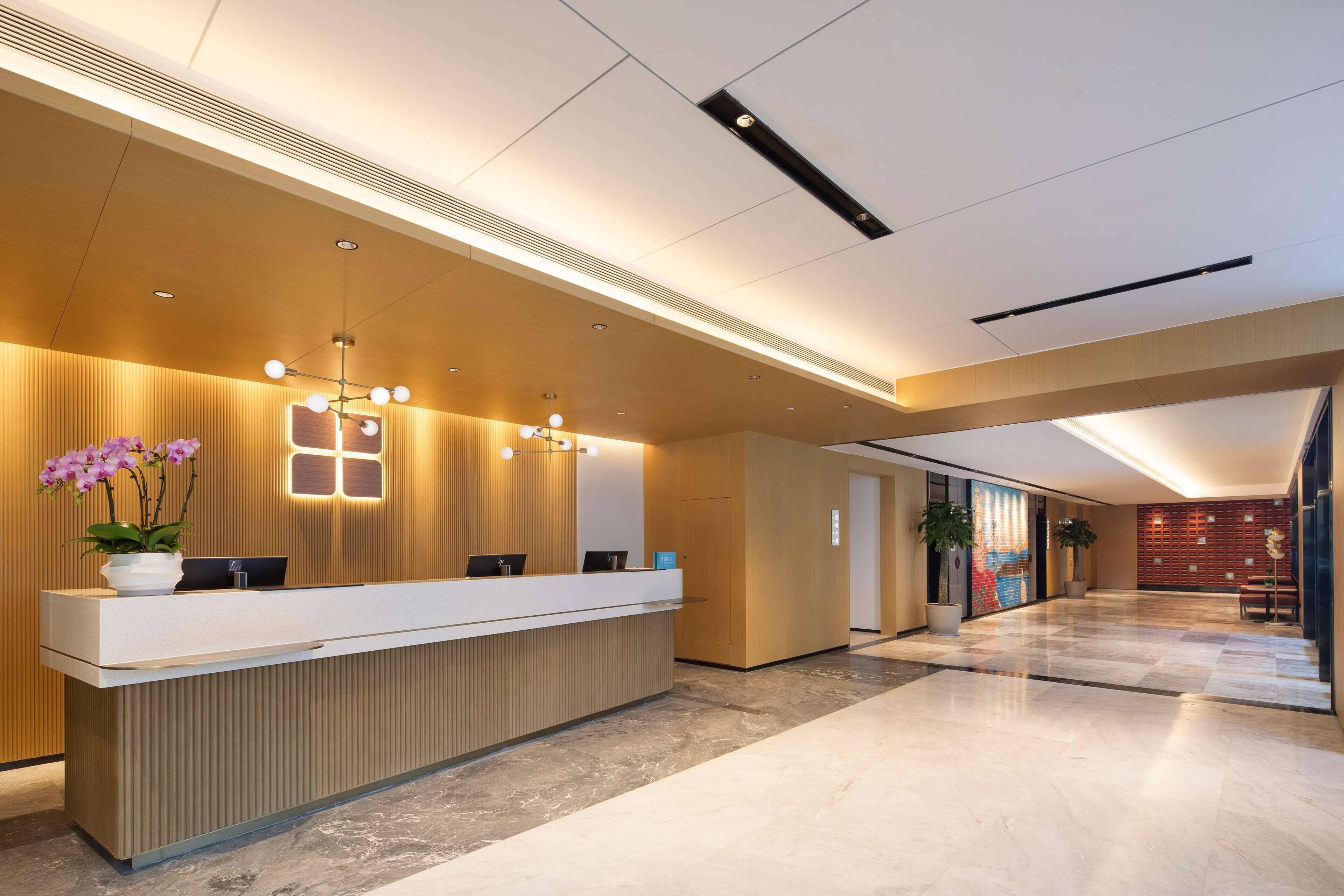 A modern reception area with a wooden reception desk, a potted plant, and a wall-mounted light fixture.