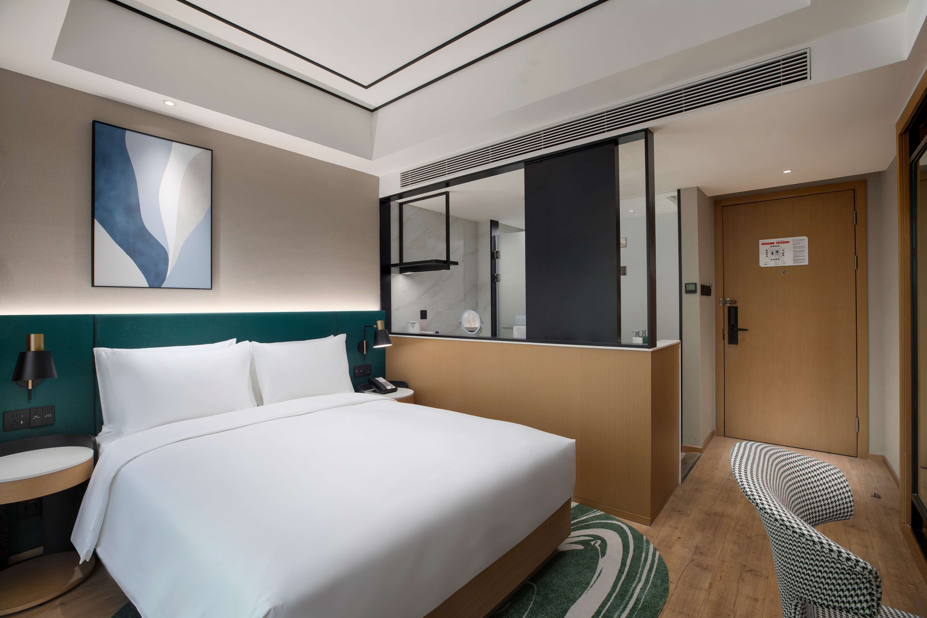 Une chambre d’hôtel avec un grand lit, une table de chevet, un miroir, un tableau décoratif au mur et une porte avec une pancarte.