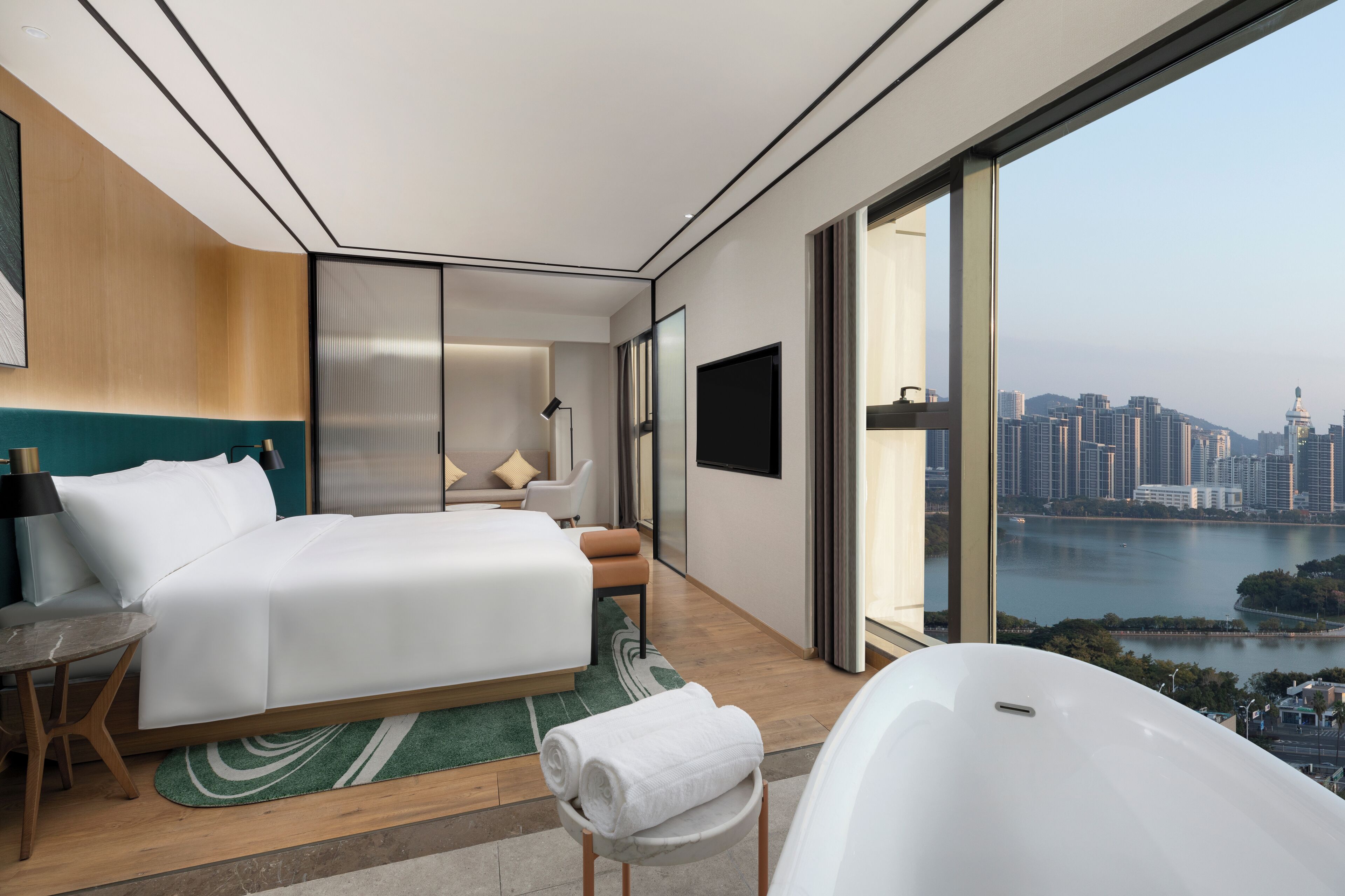 Une chambre d’hôtel moderne dotée d’un grand lit, d’un coin salon, d’une baignoire et offrant une vue sur la ville.