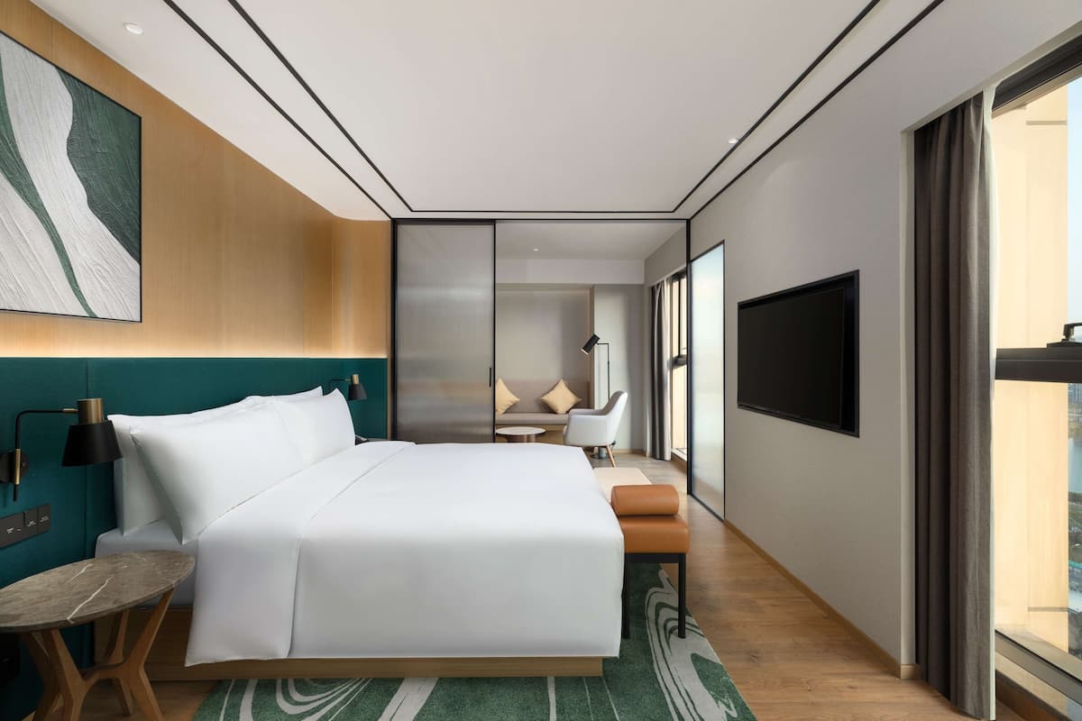 A modern hotel room with a large bed, a desk, a sofa, and a TV.