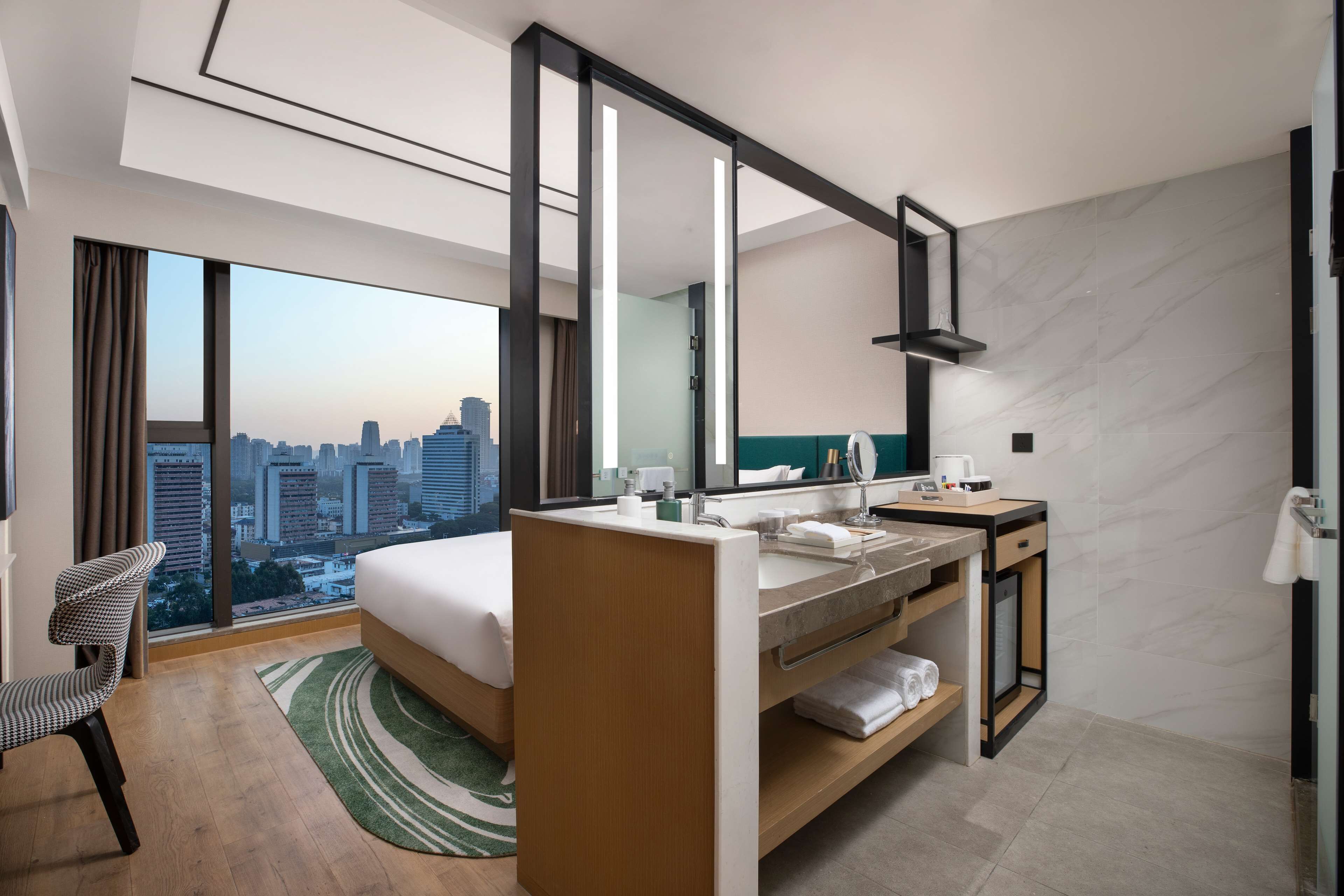 Una habitación de hotel moderna con una cama grande, un baño con tocador y vistas a la ciudad.