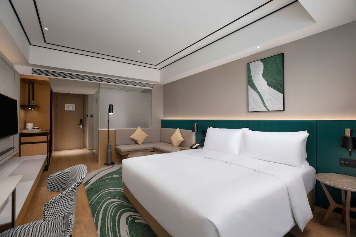A modern hotel room with a large bed, a desk, a sofa, and a TV.