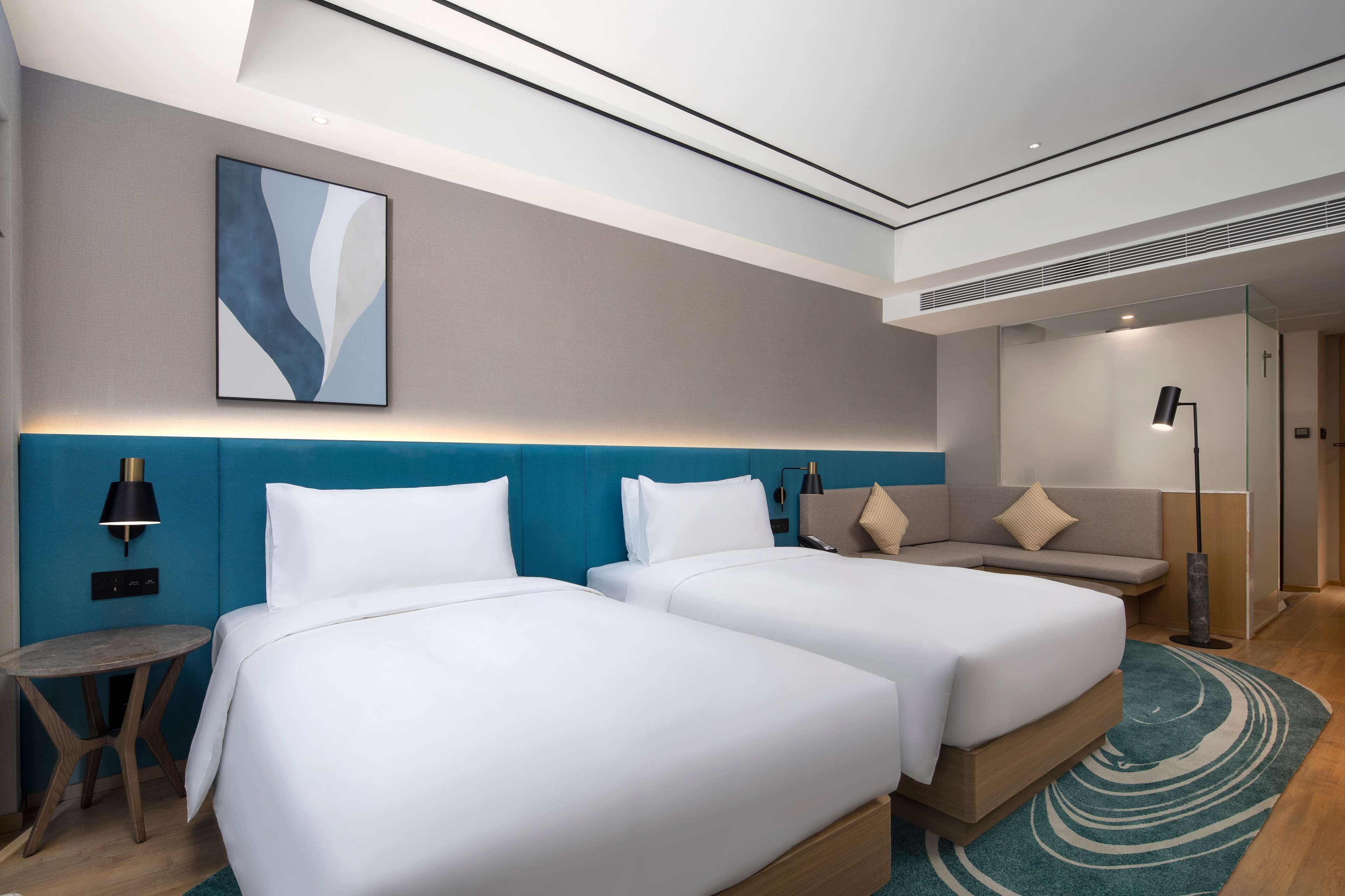 Een moderne hotelkamer met twee bedden, een bank, een kleine tafel en een groot abstract schilderij aan de muur.