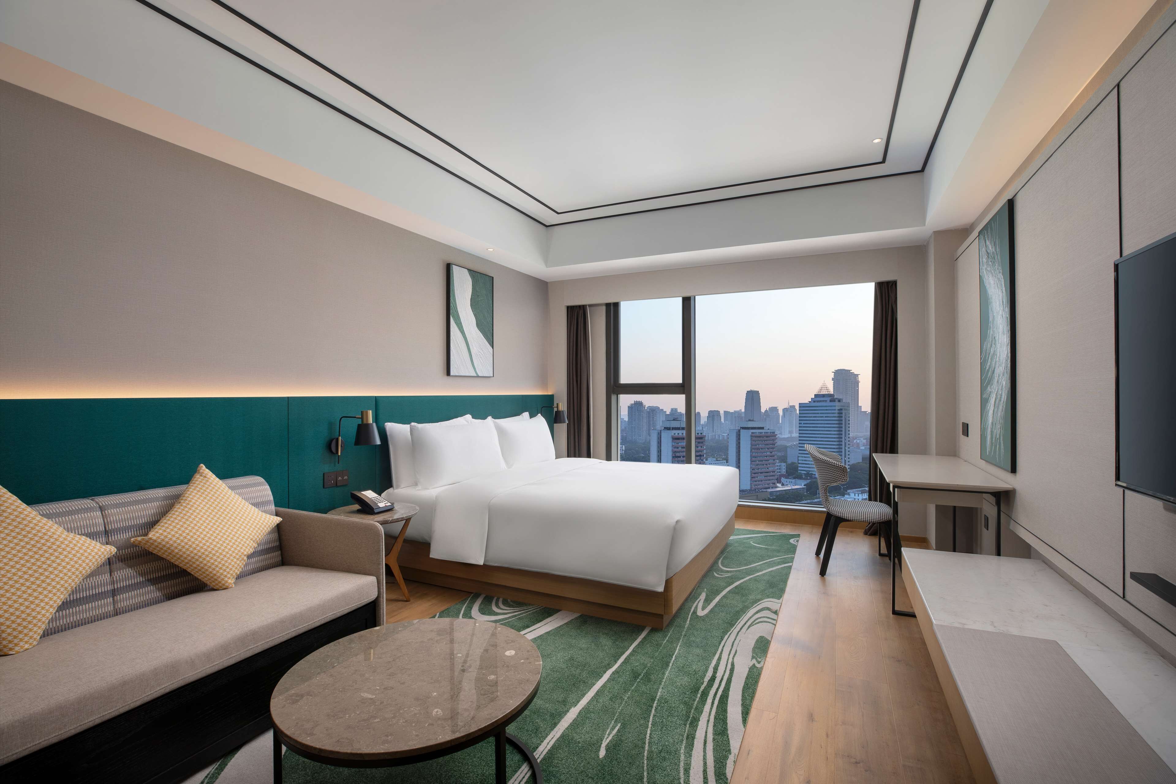 A modern hotel room with a large bed, a sofa, a small table, and a TV.