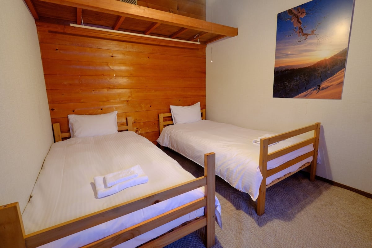 Una habitación con dos camas literas de madera, ropa de cama blanca y un cuadro de un atardecer en la pared.