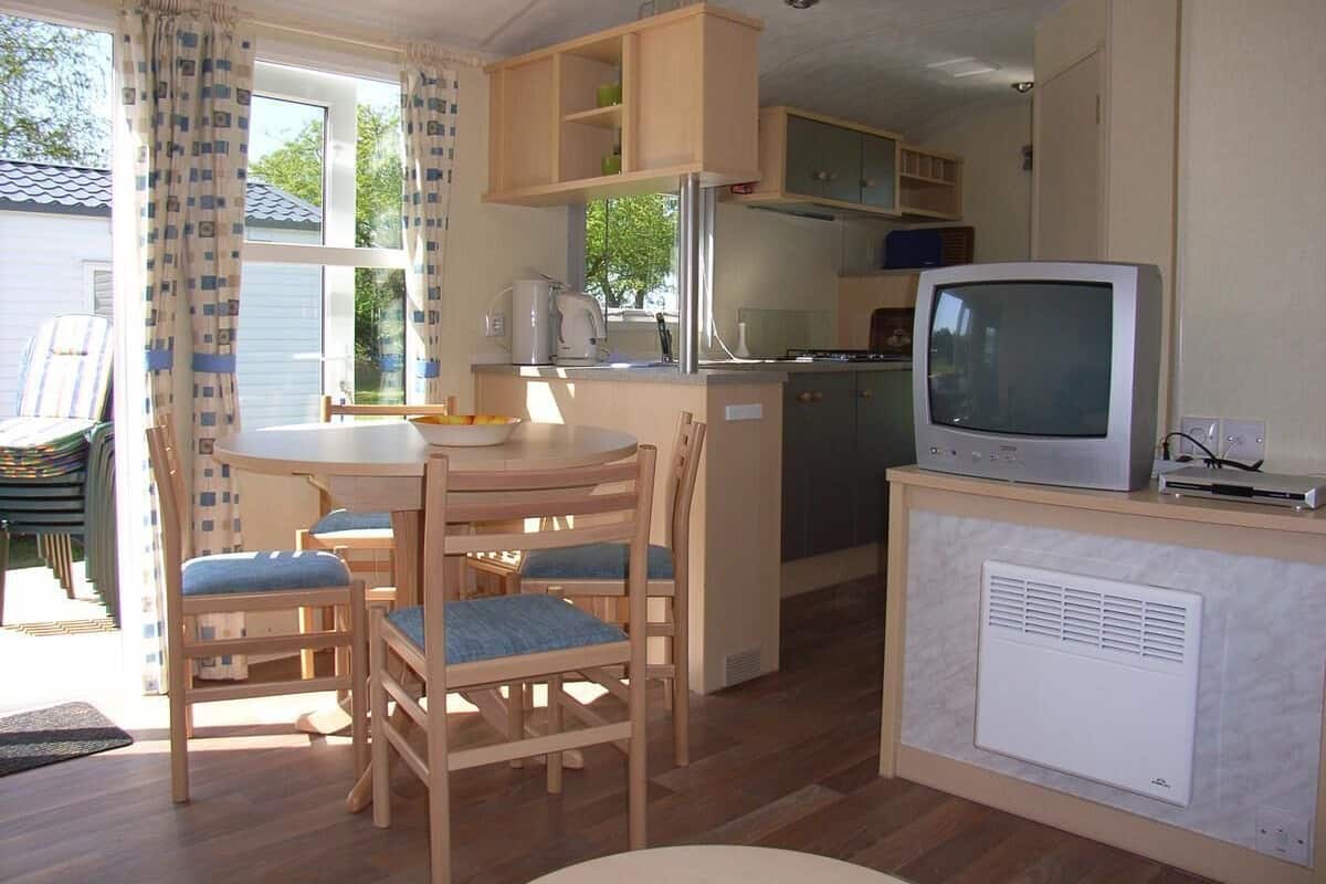 A compact kitchen with a dining area, wooden cabinets, a refrigerator, and a television.