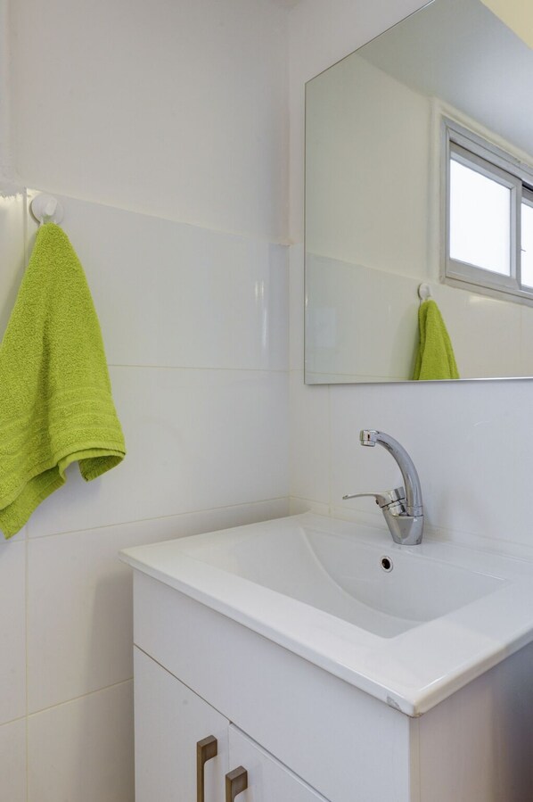 A bathroom with a white sink, a mirror, and a green towel hanging on a towel rack.