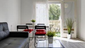 Ein modernes Wohnzimmer mit einem grauen Sofa, einem Esstisch mit Stühlen und einer Topfpflanze.